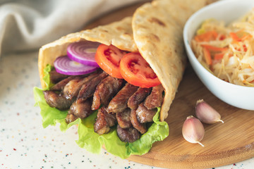 Handmade doner kebab is lying on the white table made of artificial stone Shawarma on the wooden cutting board with chicken meat, onions, salad lies on a dark old wooden table.