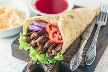 Handmade doner kebab is lying on the white table made of artificial stone Shawarma on the wooden cutting board with chicken meat, onions, salad lies on a dark old wooden table.