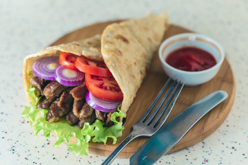 Handmade doner kebab is lying on the white table made of artificial stone Shawarma on the wooden cutting board with chicken meat, onions, salad lies on a dark old wooden table.