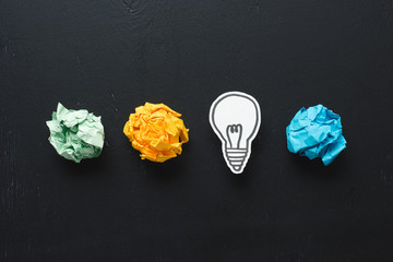top view of colorful crumpled paper balls and light bulb drawing on black background, ideas concept