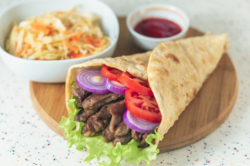 Handmade doner kebab is lying on the white table made of artificial stone Shawarma on the wooden cutting board with chicken meat, onions, salad lies on a dark old wooden table.