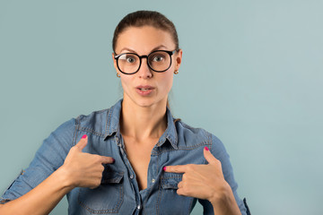 beautiful young girl in a denim shirt with glasses on a blue background with astonishment on her...