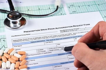 Human fill Prescription drugs prior authorization request form, pills, stethoscope on a EKG graph...