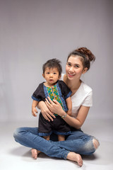 Happy young mother sitting with baby on a gray background