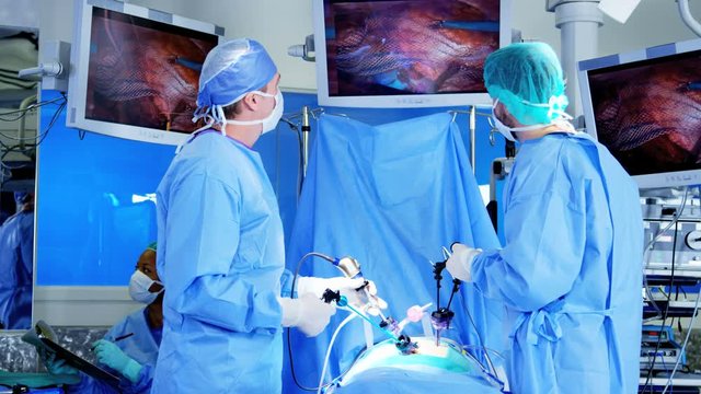 Professional Multi ethnic hospital specialist team in scrubs in the operating theatre performing Laparoscopy surgery using video monitor playback and Endoscope and Laparoscope instruments 