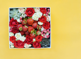 Box with small roses of different colors and berries and strawberries on a yellow background.
