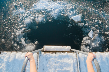 Young woman's hands holding on metallic ladder handles. Ready for swimming in ice hole at lake...