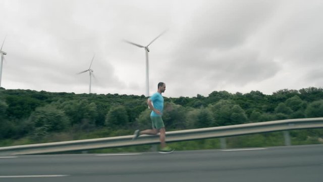 Man in blue tshirt runs along the road and operating wind turbines