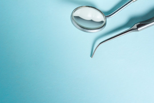 Dental mirror and explorer on blue light background with copy space, close up.