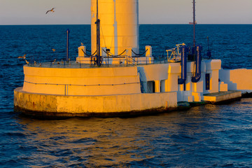 The lower part of the lighthouse at the entrance to  port on  background of a beautiful evening blue sky in soft colors. Summer seascape. White lighthouse with a red top. Black Sea. Seaport of Odessa