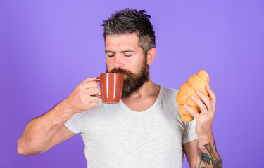 Bearded hipster enjoy breakfast drink coffee. Morning tradition concept. But first coffee. Enjoy every sip of coffee. Perfect match. Man start morning with cup of coffee and fresh croissant