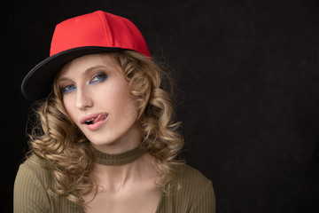 Portrait of naughty girl in red cap and with tongue. Space for text and copy-paste. Dark Studio background and a vivid portrait of the model