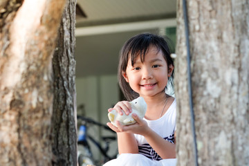 Asian cute Child girl smiling and holding a toy behind a tree