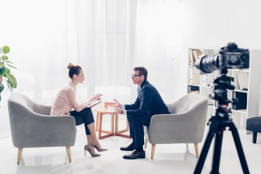 handsome businessman giving interview to journalist in office, they sitting in armchairs and looking at each other