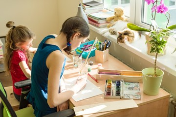 Family, recreation, creativity, home. Girls sisters at home at the table paint with watercolor.