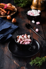Hot chocolate with marshmallow candies in black ceramic cup on old dark vintage wooden background. Selective focus.