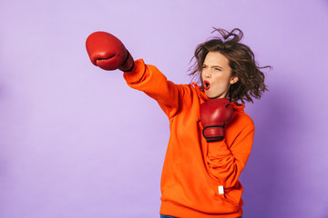 Strong young woman boxer posing isolated over purple background wall wearing boxing gloves.