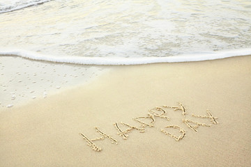 handwritten inscription happy day made in the sand near the water, the wave washes text on the beach