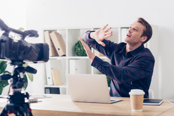 shocked male video blogger recording vlog and showing stop sign in office