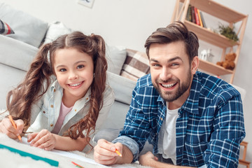 Obraz premium Father and little daughter at home lying on floor holding pencils looking camera happy close-up