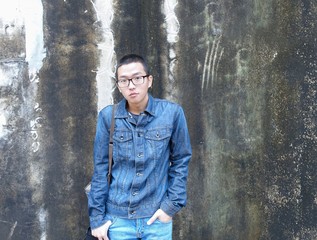 Fototapeta na wymiar Handsome asian CASUAL JEANS glasses man posing on wall with lichen background. Portrait of young KOREAN against dirt concrete wall background.