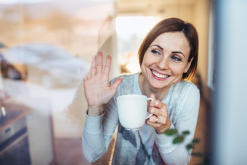 A young woman with cup of coffee looking out of a window, waving goodbye.