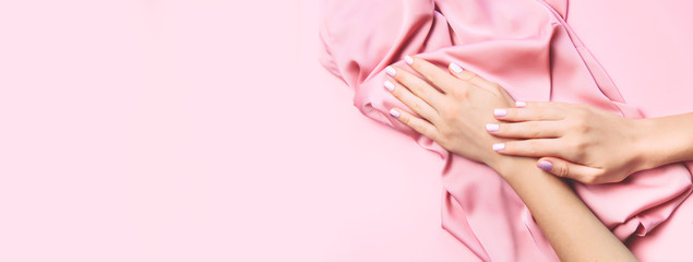 Beautiful woman manicure on creative pink background with silk fabric. Minimalist trend.