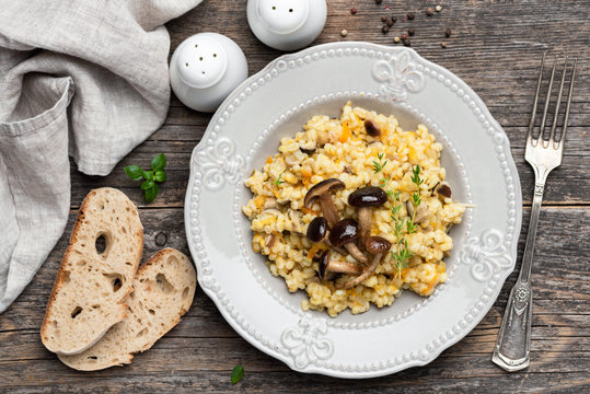 Pearl barley risotto with mushrooms on wooden background. Top view