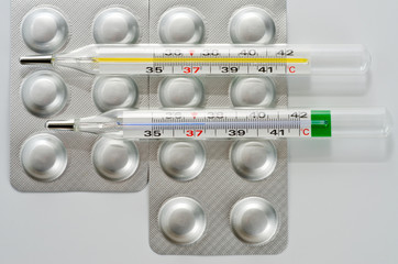 Plate with round medical tablets of silver color and glass thermometer