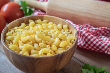 Raw macaroni pasta in wooden bowl