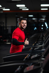Man in sportswear running on treadmill at gym in red clothes