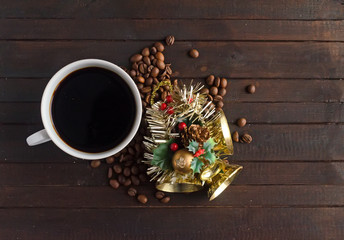 A cup of coffee, coffee beans and Christmas toy with three golden bells on dark wooden background.Christmas concept.