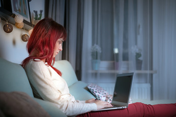 Young woman using laptop while sitting on sofa at evening