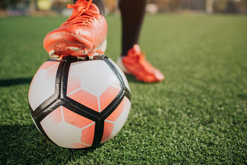 Pictre of man's leg on football ball. Another one stand on green lawn. It is sunny outside.