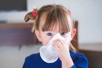little girl blowing her nose into a handkerchief.