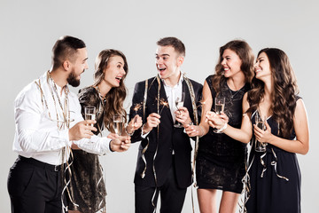 Company of  girls and guys dressed in stylish elegant clothes have fun together holding glasses of champagne and sparkles in hands on the white background confiture around. Party time