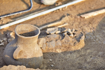 Real archaeological excavation. The remains of human bones and well-preserved clay jar finding in the ground. Outdoors, close up, copy space.