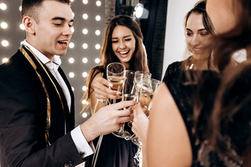 Сompany of happy friends dressed in stylish elegant clothes stand together and clink glasses with champagne. Party time