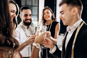 Сompany of beautiful young girls and guys dressed in stylish elegant clothes stand together and clink glasses with champagne. Party time