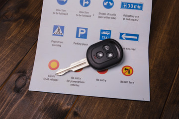Concept - driving instruction. Closeup of road signs and car keys on a wooden background.