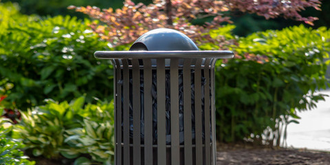Outdoor trash can with plants in the background