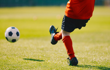 Young Football Player Kicking Ball on the Soccer Pitch. Boy Wearing Red Sports Jersey, Black...