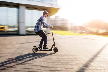 Foto op Plexiglas Young man in casual wear on electric kick scooter on city street in motion blur in sunday © bortnikau