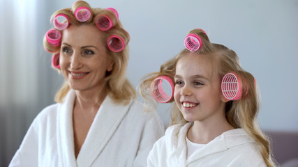 Elderly lady and little girl looking in mirror and enjoying rolling hair, style