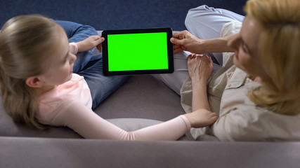 Little girl and grandmother holding tablet with green screen, modern technology - Powered by Adobe