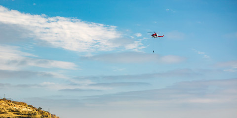 Person hanging on chopper above cliff in La Jolla
