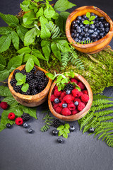 Freshly assorted berries in wooden bowl. Juicy and fresh blueberries6 blackberries and raspberries with green leaves on rustic background. Concept for healthy eating and nutrition.