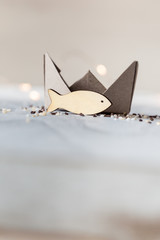 Kleiner Fisch aus Holz mit Schiffchen aus Papier als Symbol für Glaube, Reise, Ankunft
