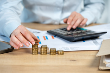 Close up cropped investor or sale manager lady in her formal wear shirt she put money in pile sit behind table in bright loft interior workstation count tax on invoice focus on hand with coins