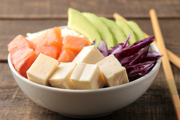 poke bowl Hawaiian food. plate with rice, salmon, avocado, cabbage and cheese, on a brown wooden table